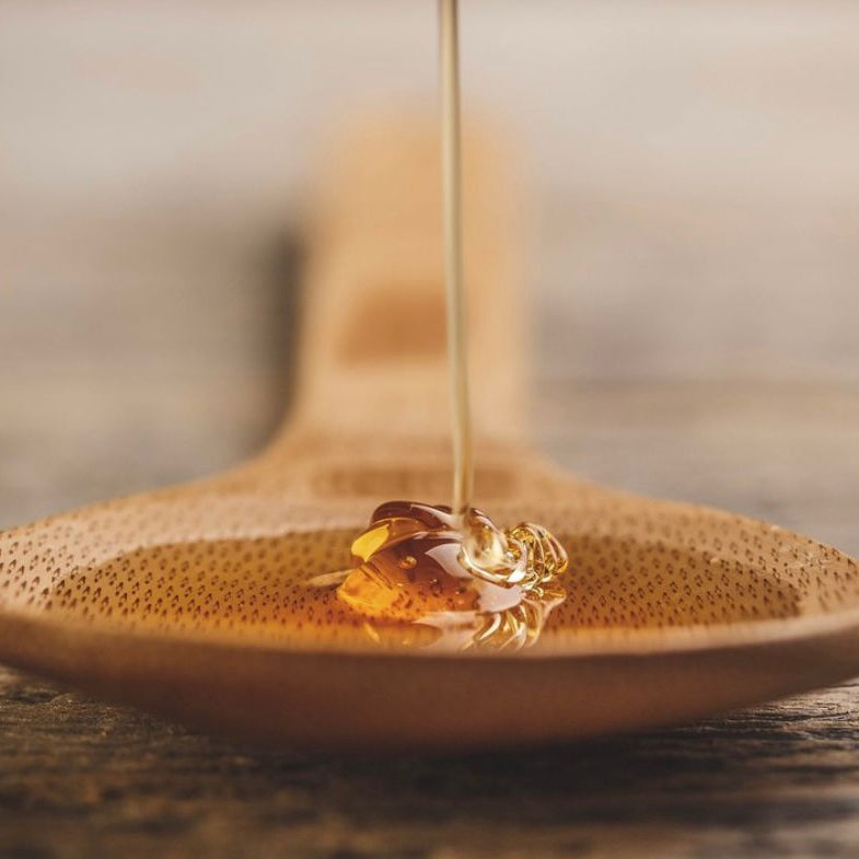 Honey being drizzled onto a wooden spoon with a blurred background