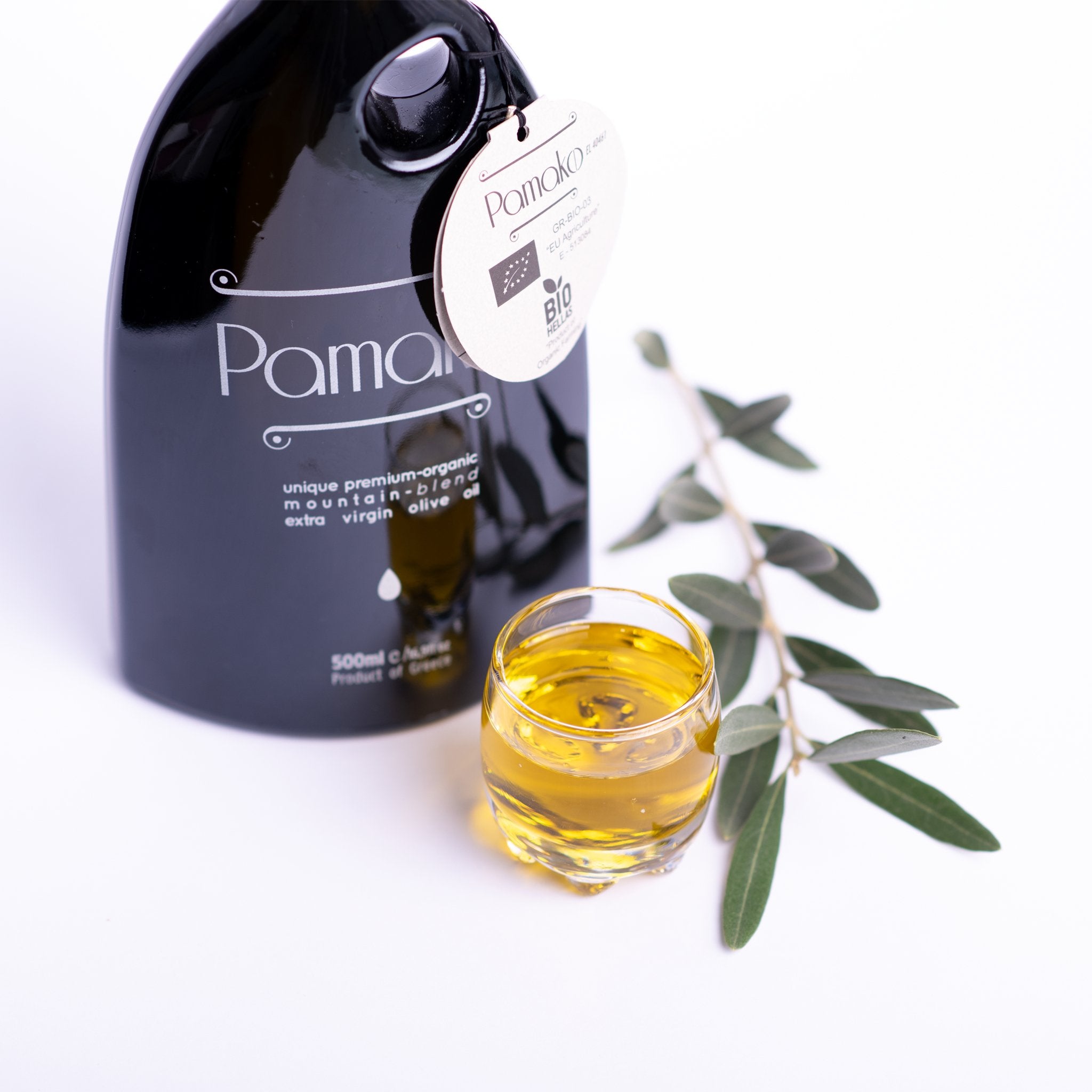 Pamako Blend EVOO in a transparent glass with olive leaves aside. 