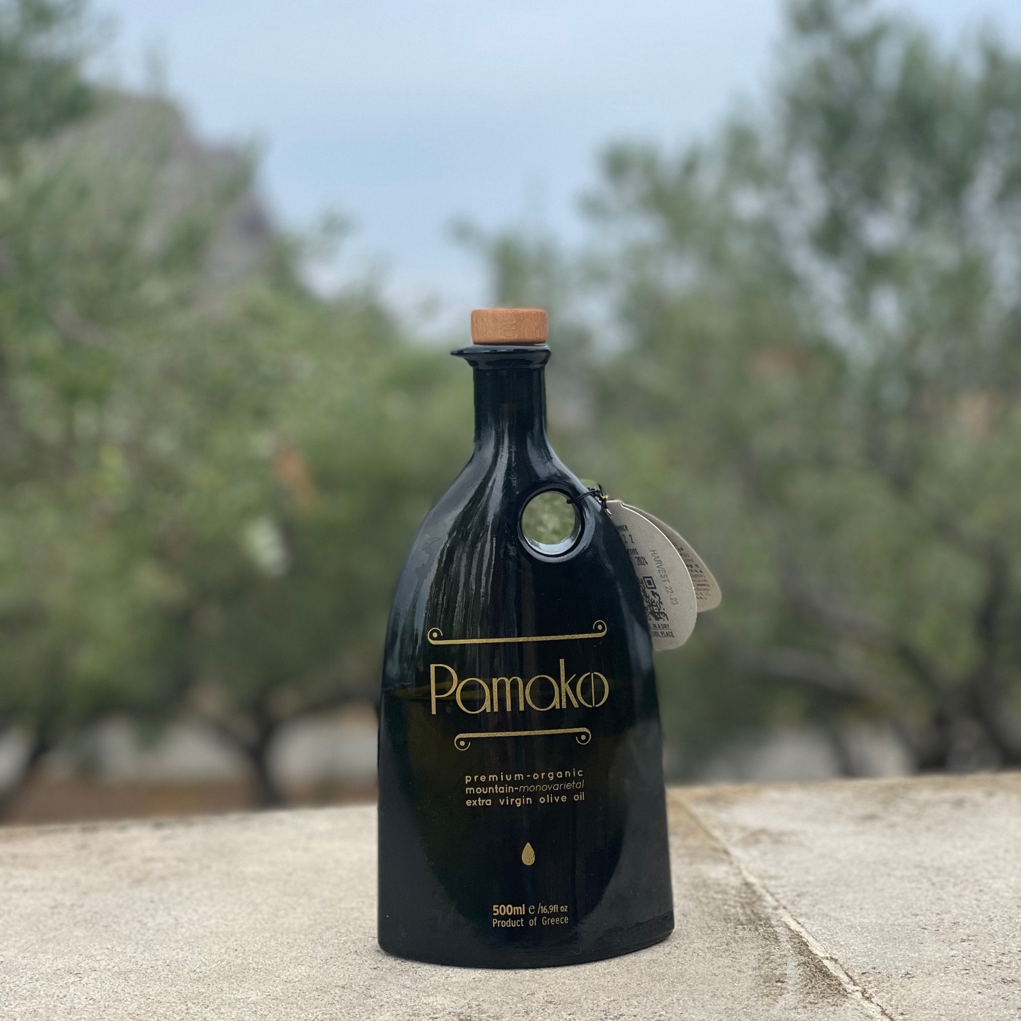 A bottle of Pamako Monovarietal olive oil with olive trees in the back and wooden cork.